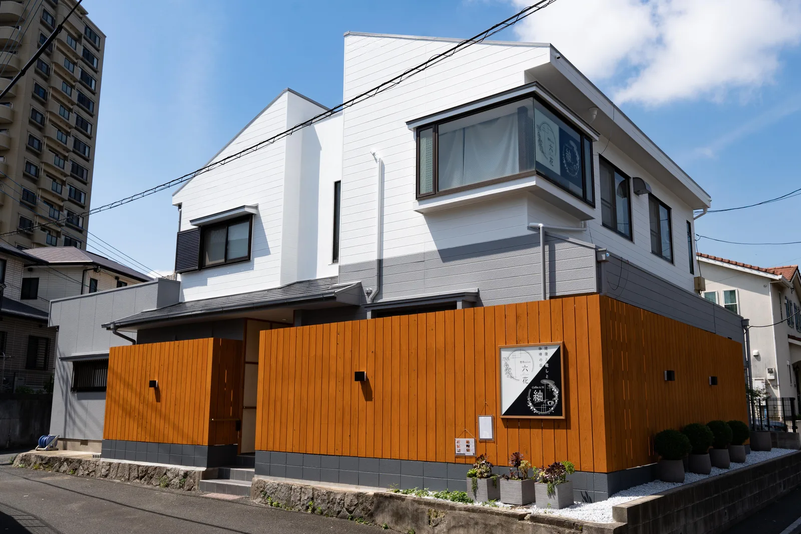 木張りの外壁に看板が掛かる、白と木目の建物の外観